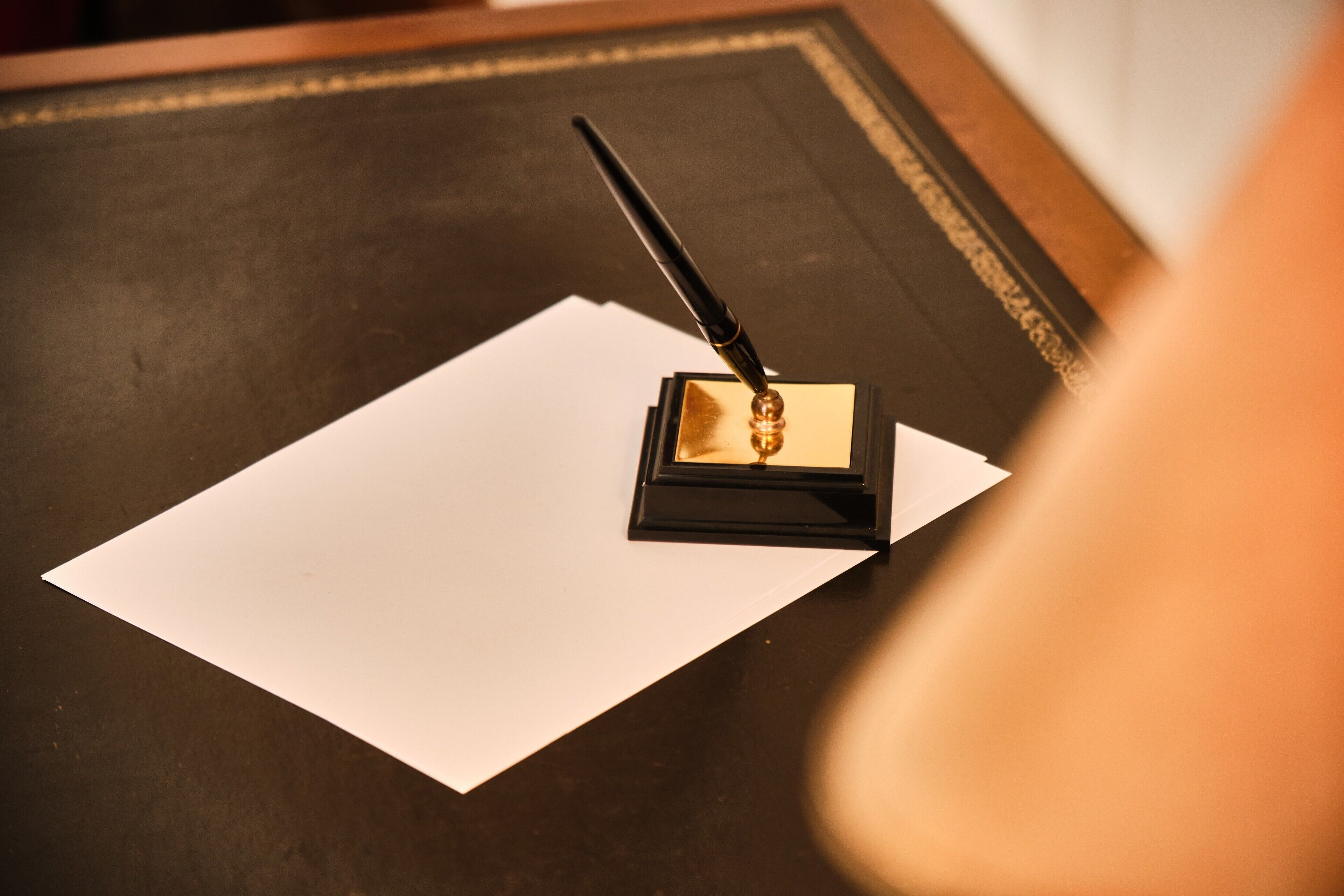 A black desk with a white sheet of paper and a pen on top.