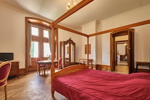 A bedroom with a four-poster bed, wooden furniture, a television, and a dining area with chairs and a table.