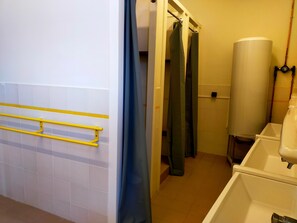 Ein Badezimmer mit einer gelben Handstange, einer Duschvorhang, einem weißen Waschbecken und einem großen zylinderförmigen Boiler.