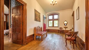 A room with wooden flooring, a bench, a table with chairs, a chandelier, and a large window.