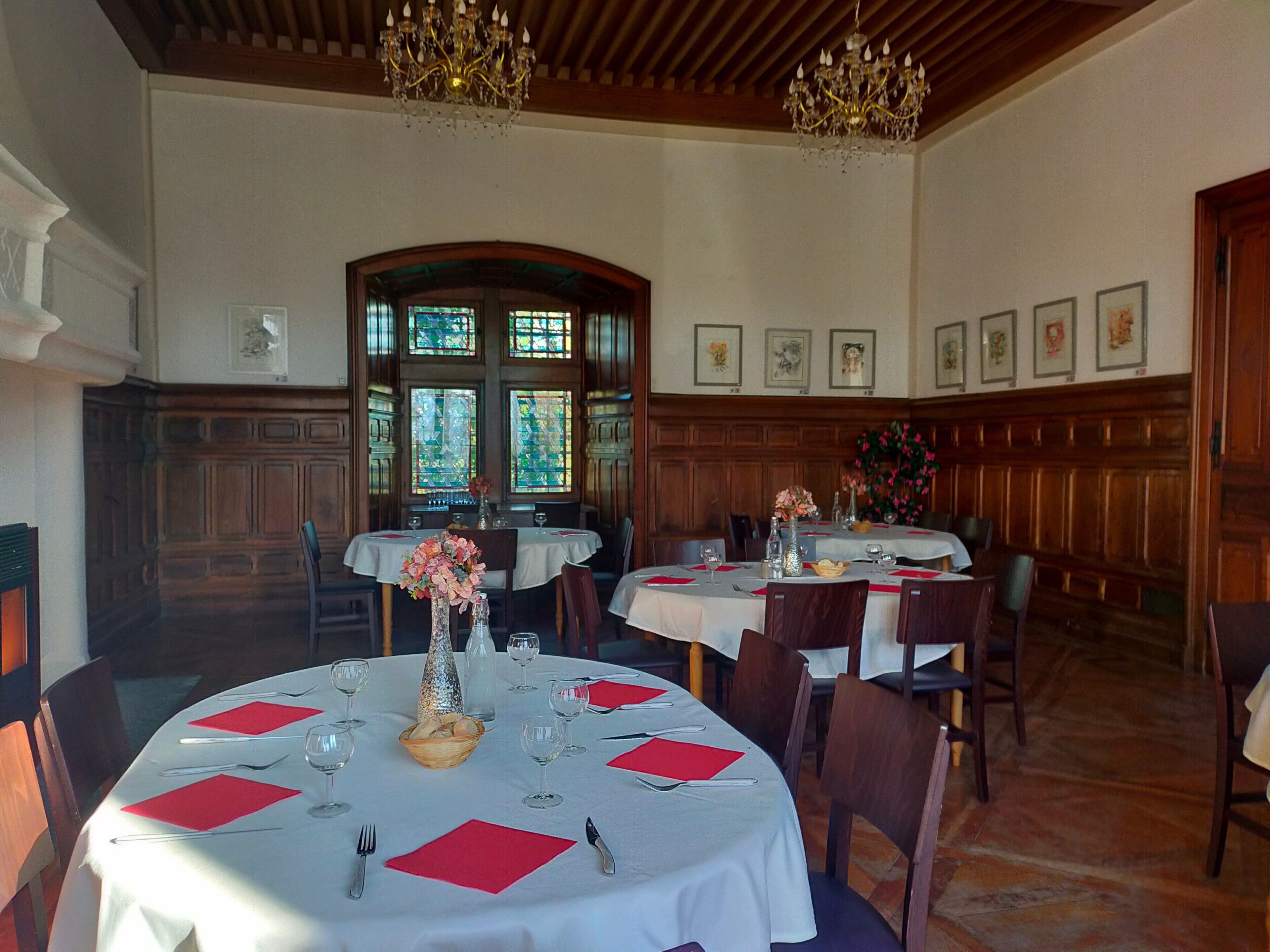 Un espace repas avec des tables rondes, des chaises, des lustres et des vitraux.