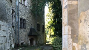 Un estrecho callejón entre edificios de piedra, con un sendero de grava, un pequeño arco de entrada y una ventana con barrotes.