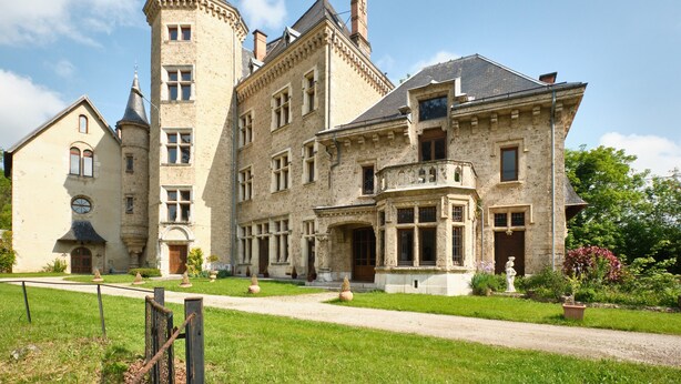 A large, historic building with a prominent tower, multiple windows, and a well-maintained lawn.