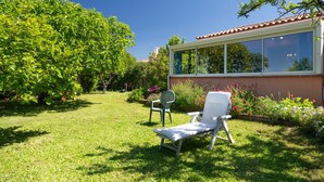 Un jardín con césped, una silla de lounge blanca, una silla verde y un edificio con una ventana.