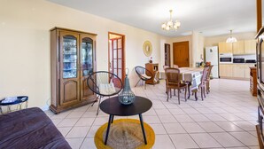Una sala de estar con sofá, una mesa de comedor con sillas, un mueble bar con puertas de vidrio y una zona de cocina con armarios y electrodomésticos.