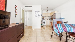 A modern kitchen with a microwave, refrigerator, and washing machine. There is a dining table with a striped tablecloth and a television on a cabinet. - Apartment 'Superbe Appartement Vue Mer' with Sea View, Wi-Fi and Air Conditioning (Fréjus)