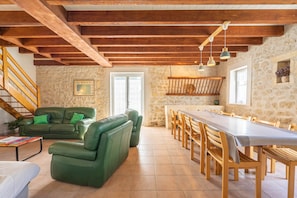 A spacious room with a dining table, wooden chairs, a green sofa, and a staircase.