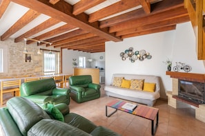 A spacious living area with a stone wall, wooden beams, a fireplace, and a dining area with chairs and a table.
