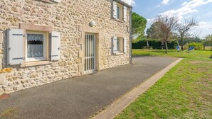 Un bâtiment en pierre avec une allée pavée et une zone herbeuse équipée d’installations de jeux pour enfants.