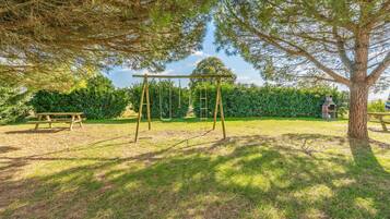 A park with a swing set, picnic table, and a large tree.