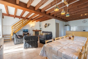 A spacious living area with a high ceiling, wooden beams, a dining table set, leather sofas, and a television.