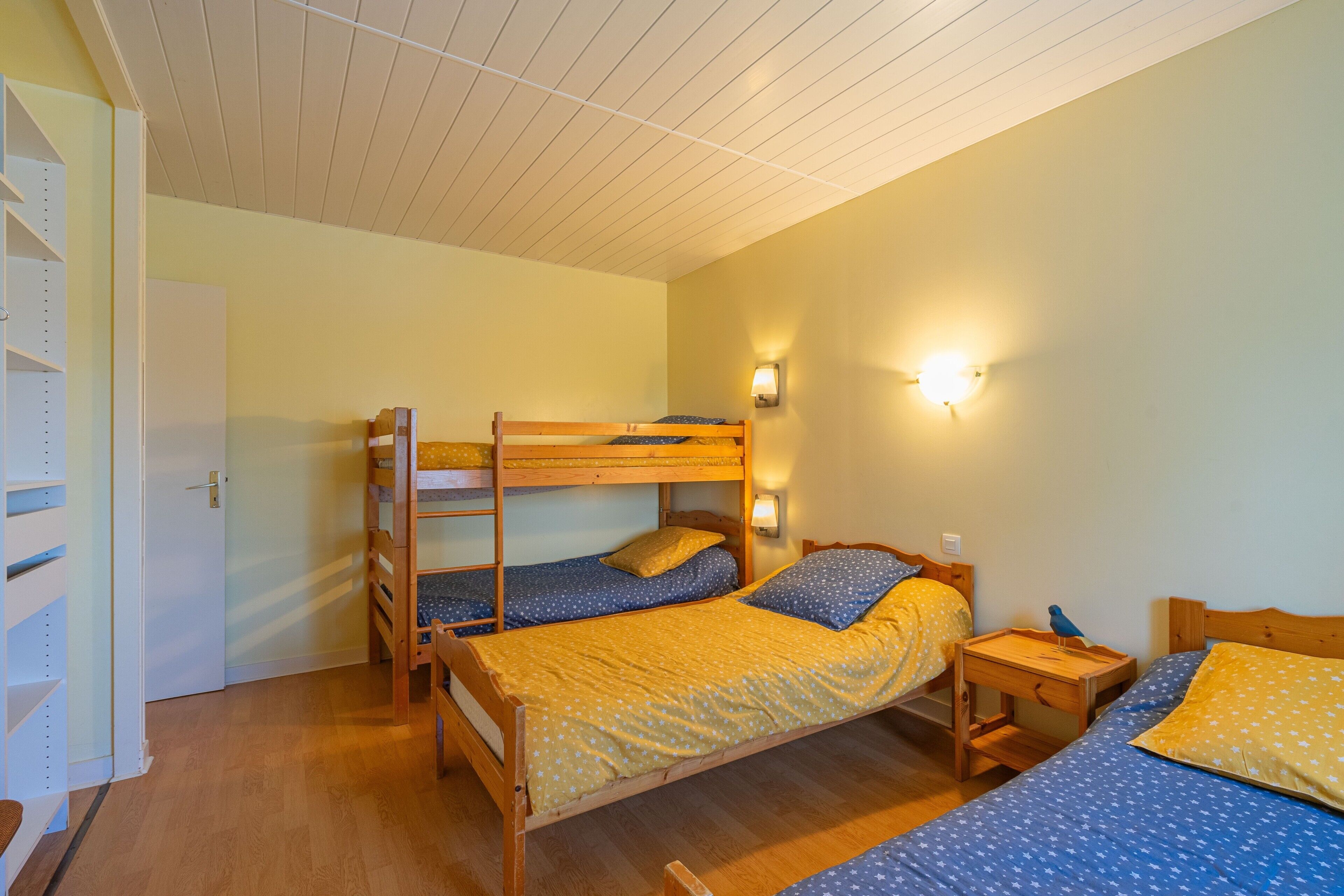 Habitación con literas, suelo de madera, puerta blanca y lámpara fijada a la pared.