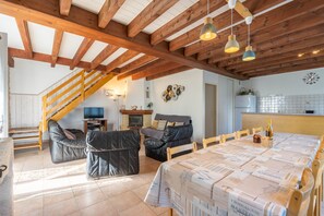 A spacious living area with a high ceiling, wooden beams, a dining table with a patterned tablecloth, leather sofas, and a staircase leading to an upper level. - Group Gite with Indoor Pool, Private Terrace, Garden, and Wi-Fi (La Gripperie-Saint-Symphorien)
