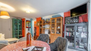 A living room with a table, chairs, a bookshelf, and a television. - Apartment 'Le Grand Lapin Blanc' with Sea View, Private Terrace and Wi-Fi (Fleury)