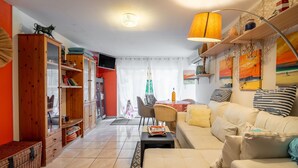 A living room with a sofa, a coffee table, a bookshelf, and a dining area with a table and chairs. - Apartment 'Le Grand Lapin Blanc' with Sea View, Private Terrace and Wi-Fi (Fleury)