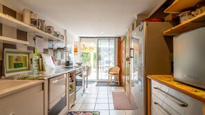 A modern kitchen with white cabinets, a refrigerator, and a dining area with a chair. - Apartment 'Le Grand Lapin Blanc' with Sea View, Private Terrace and Wi-Fi (Fleury)