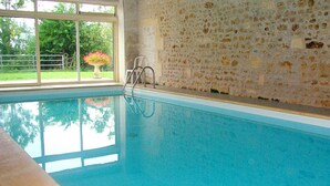 Una piscina interior con paredes de vidrio transparente, un muro de piedra y una escalera de metal.
