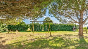 Un parque con columpios, una mesa de picnic y un árbol grande.