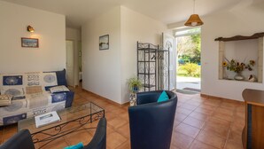 Un salón con un sofá, sillas, una mesa de centro de vidrio y una puerta que da a un jardín.