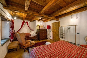 A bedroom with a wooden ceiling, a bed with a red and white checkered bedspread, a wooden chair, a wooden dresser, and a red lamp.