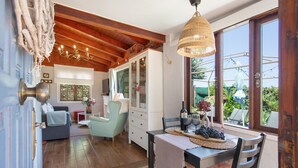 A cozy interior with a dining area, a sofa, and a view through large windows.