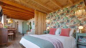 A bedroom with a wooden ceiling, a floral wallpaper, a bed with pink and white bedding, and a nightstand with a lamp.