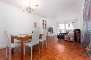 Un coin repas avec une table en bois et des chaises blanches, un buffet blanc aux portes vitrées, un téléviseur et un grand tableau abstrait accroché au mur.