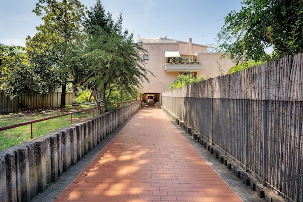 Un chemin menant à un bâtiment doté d’un balcon, entouré d’arbres et d’une clôture en bambou.