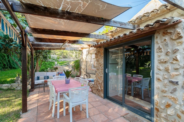 An outdoor patio with a table and chairs, a pergola, and a stone wall.