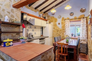 A rustic kitchen with stone walls, wooden beams, and a dining area with a table and chairs.