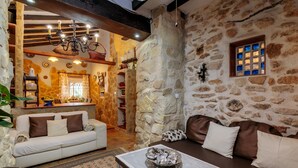 A rustic interior with stone walls, a white sofa, a brown sofa, a marble table, and a chandelier.