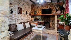 A stone-walled room with a sofa, a television, a fireplace, and a ceiling fan.