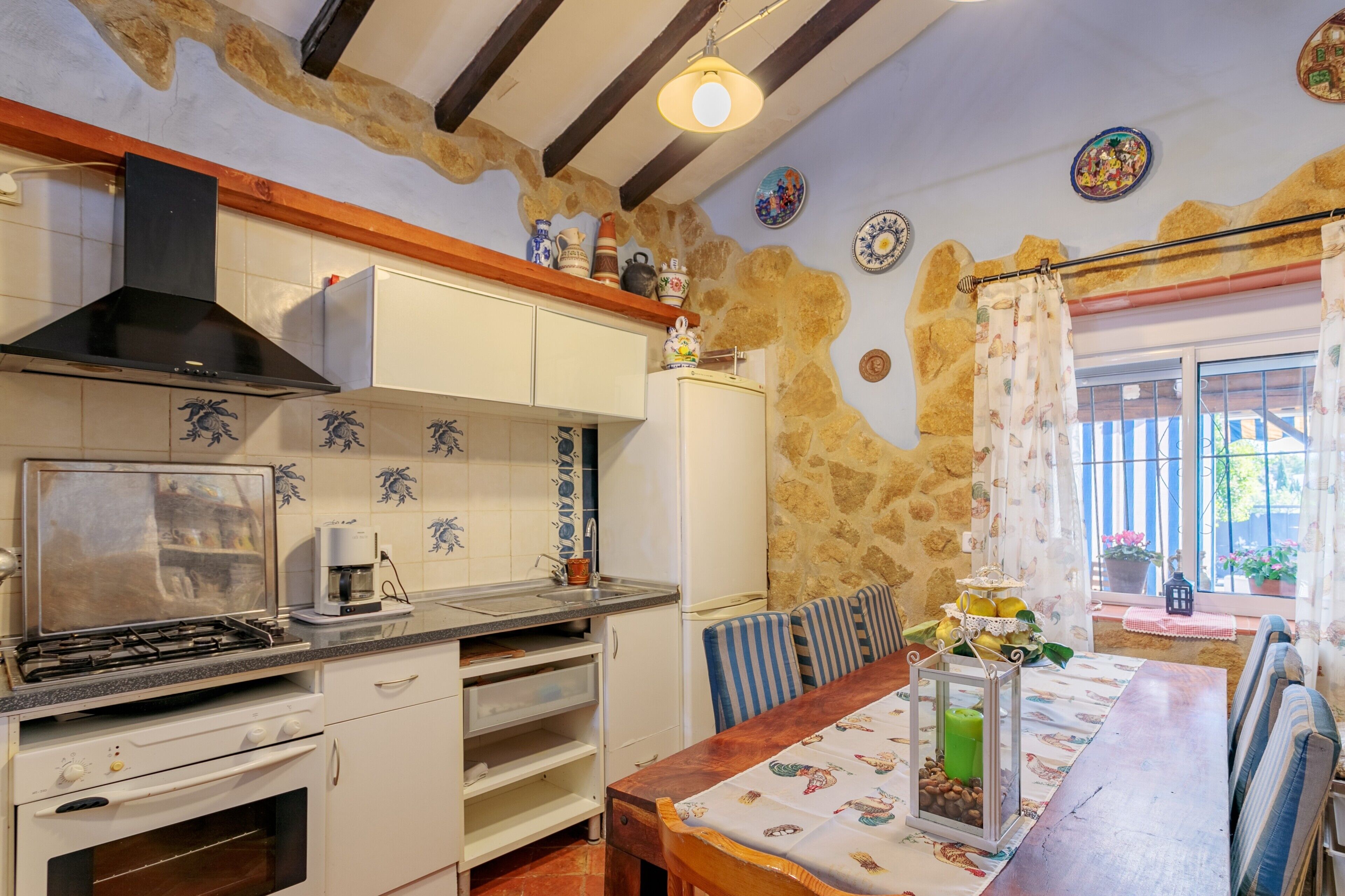 A kitchen with a stove, oven, and cabinets, a dining table with chairs, and a stone wall.