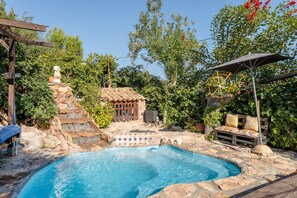 A swimming pool with a stone waterfall, a wooden deck, and a bench with cushions.