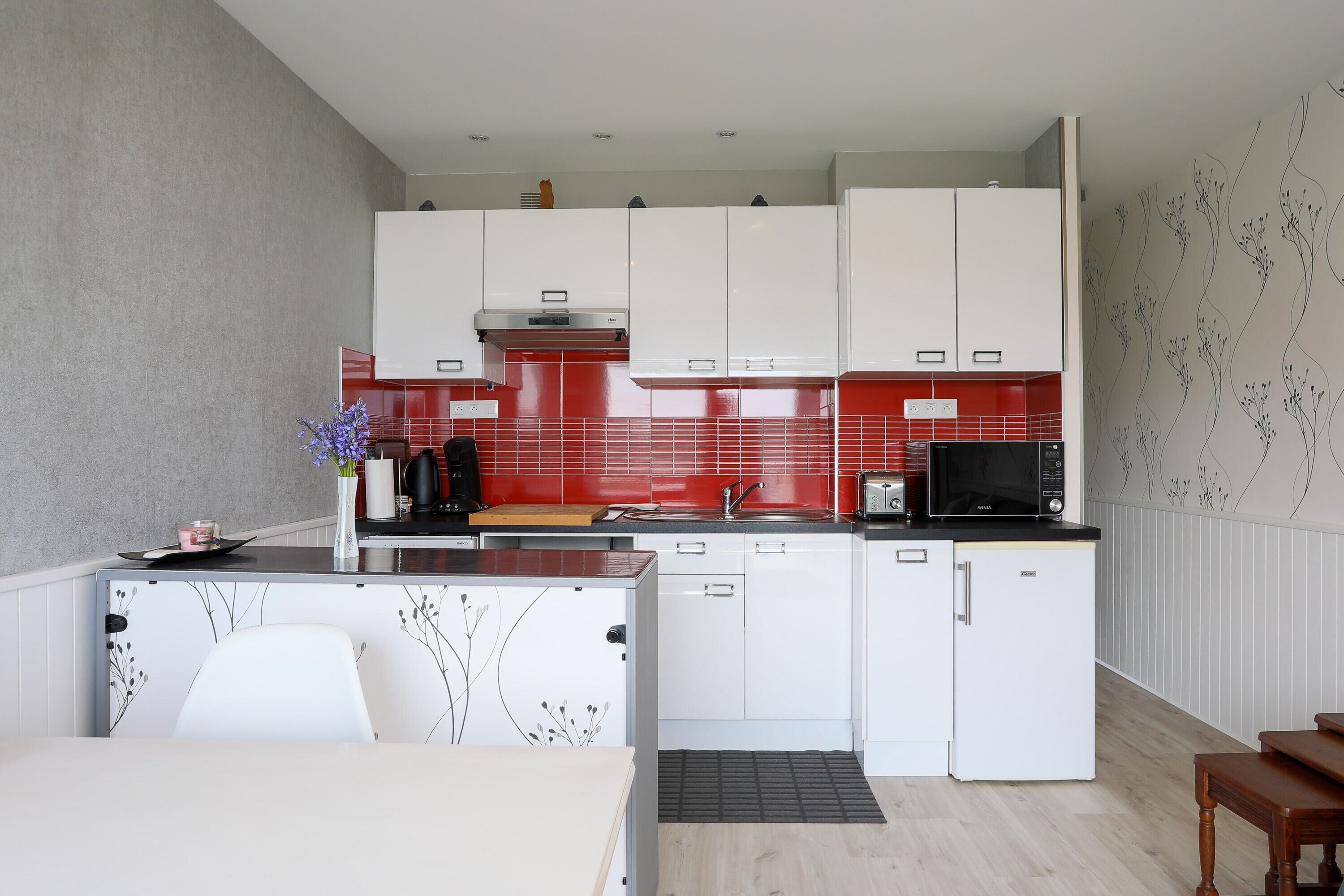 Een moderne keuken met witte kastjes, een rode achterwand en een zwarte magnetron.