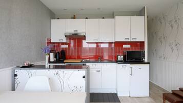Een moderne keuken met witte kastjes, een rode achterwand en een zwarte magnetron.