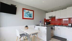 Une cuisine moderne avec des armoires blanches, un four encastré et un coin repas comprenant une table et des chaises blanches.