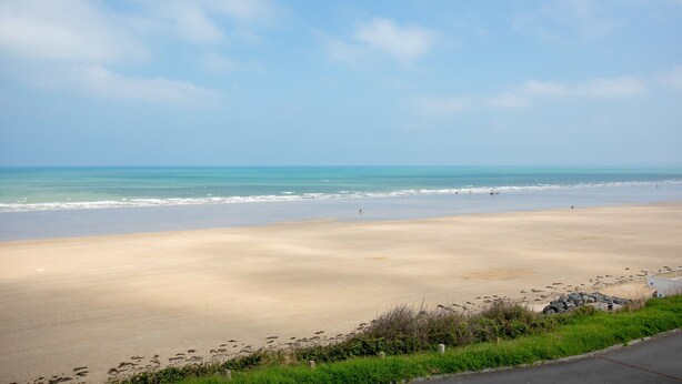 Une plage avec un ciel dégagé, une mer calme et un chemin pavé menant à la rive.