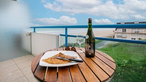 Une table en bois sur laquelle se trouvent une assiette de nourriture, une bouteille de vin et une paire de lunettes de soleil, le tout placé sur un balcon donnant sur une plage.