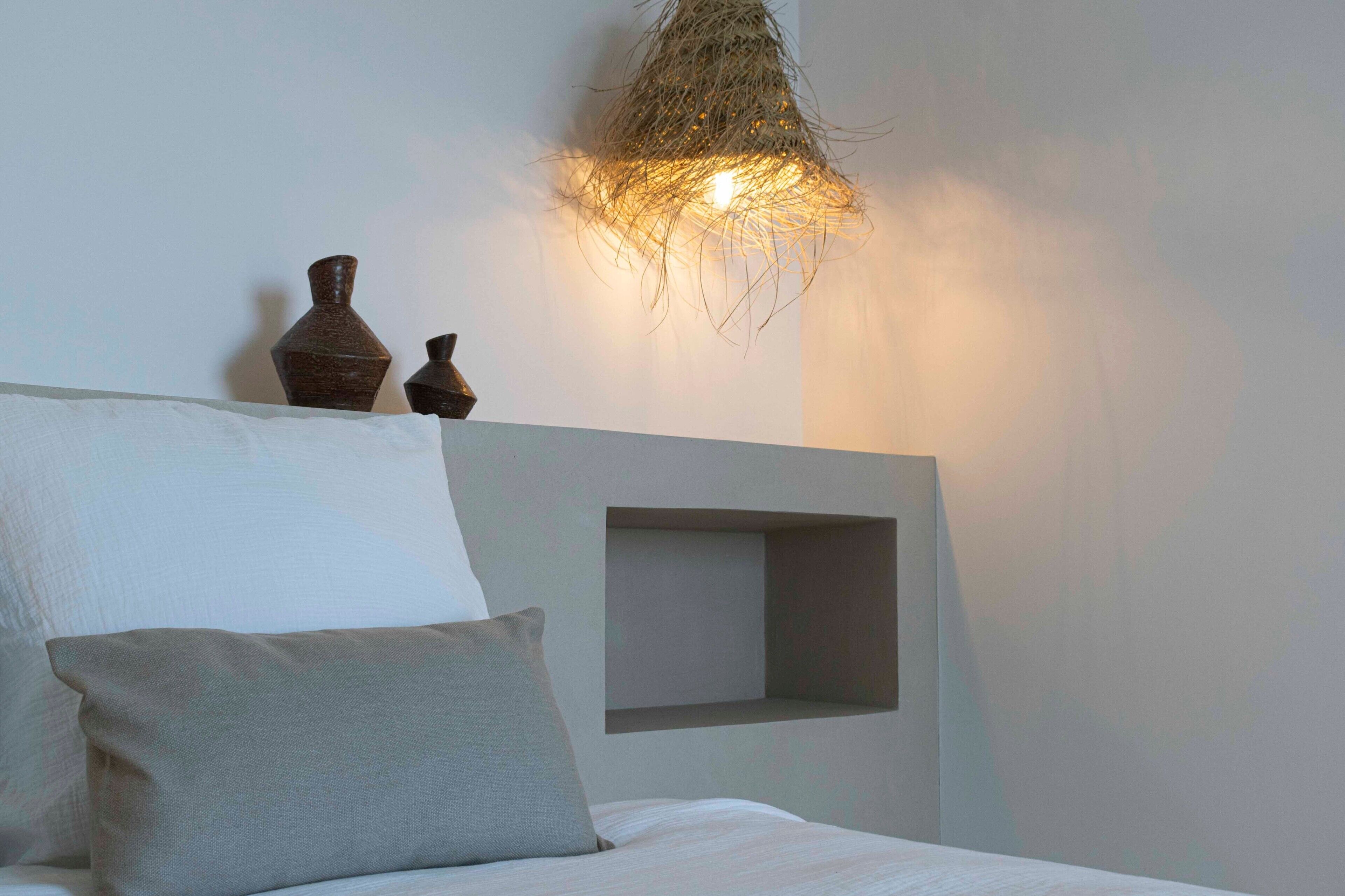 Un dormitorio con una cama, almohadas, un estante en la pared y una lámpara colgante original.