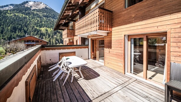 Une cabane en bois dotée d’un balcon, d’une table et de chaises, offrant une vue sur une montagne boisée.