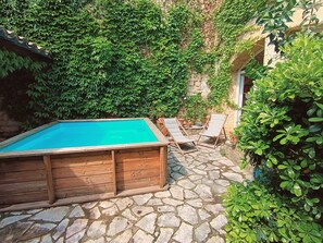 A wooden pool with stone flooring, surrounded by lush greenery and a stone wall.