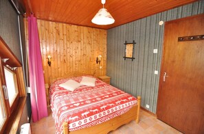 A wooden-paneled room with a bed, two wall-mounted lamps, a door, and a window with a curtain.
