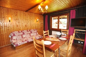 A wooden interior with a sofa, dining table, chairs, and a TV.