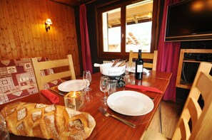 A wooden interior with a dining table set for two, a bread loaf, a bottle of wine, and a flat-screen TV.