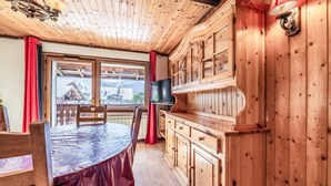 A wooden interior with a dining table, chairs, a television, and a view of a mountain.