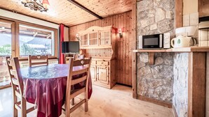 A wooden interior with a dining table, chairs, a stone wall, a microwave, and a coffee maker.
