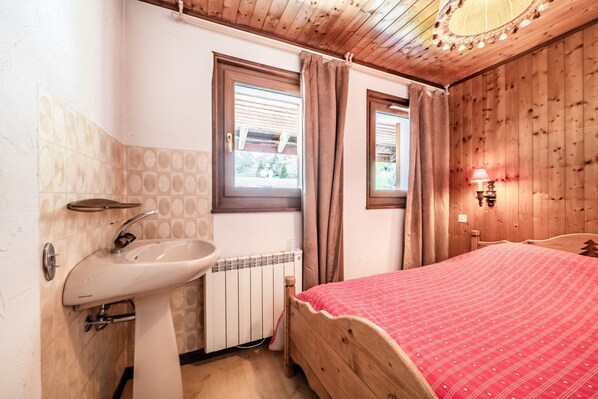 Une chambre à coucher avec un lit en bois, un lavabo blanc et une fenêtre avec des rideaux.