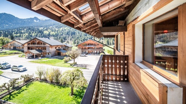 A wooden balcony with a view of a mountain landscape, a wooden building with a balcony, and a clear sky.