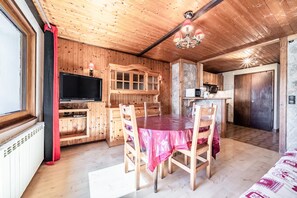 Un intérieur en bois comprenant une table à manger, des chaises, un téléviseur et un coin cuisine.